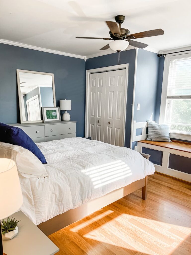 bedroom with blue walls and white comforter and grey dresser and window seat