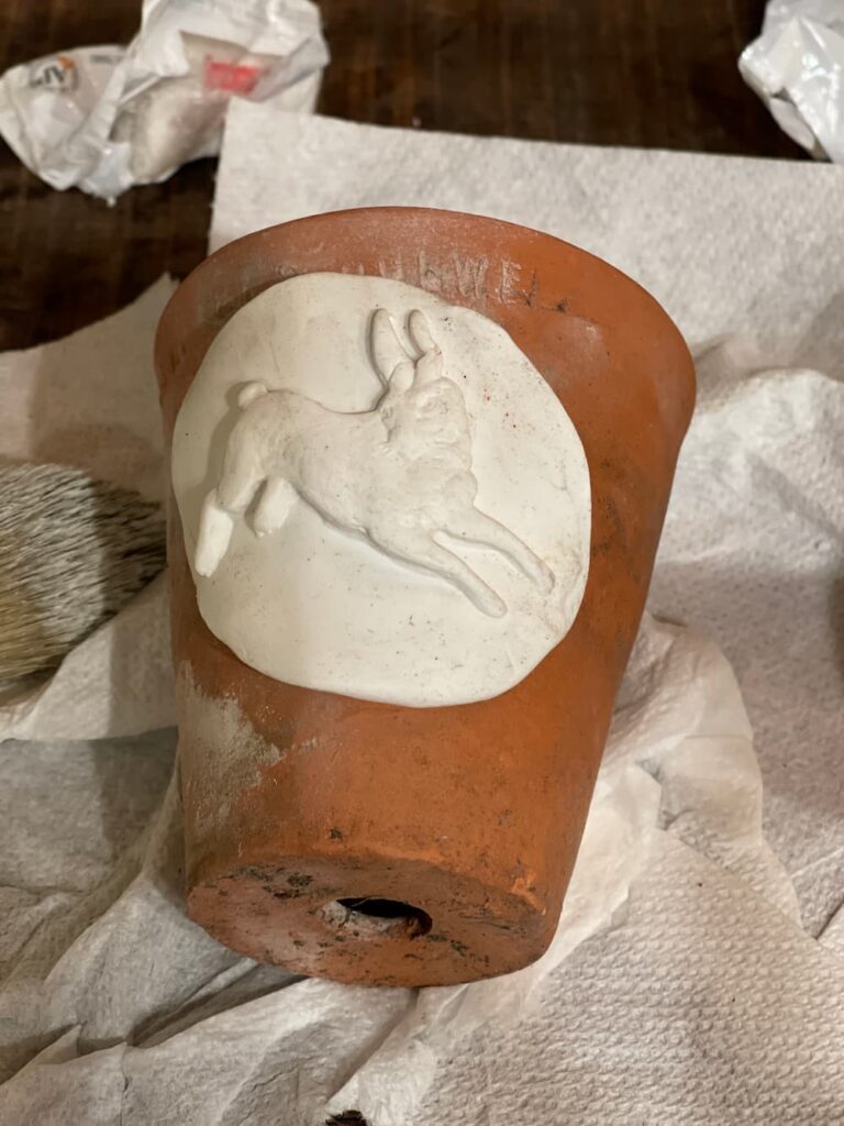 white sculpey bunny on round disc drying on side of a clay pot