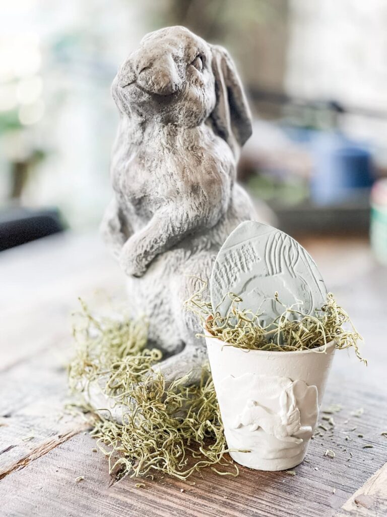 large cement bunny behind a small clay pot with a bunny imprint then filled with a stamped clay egg