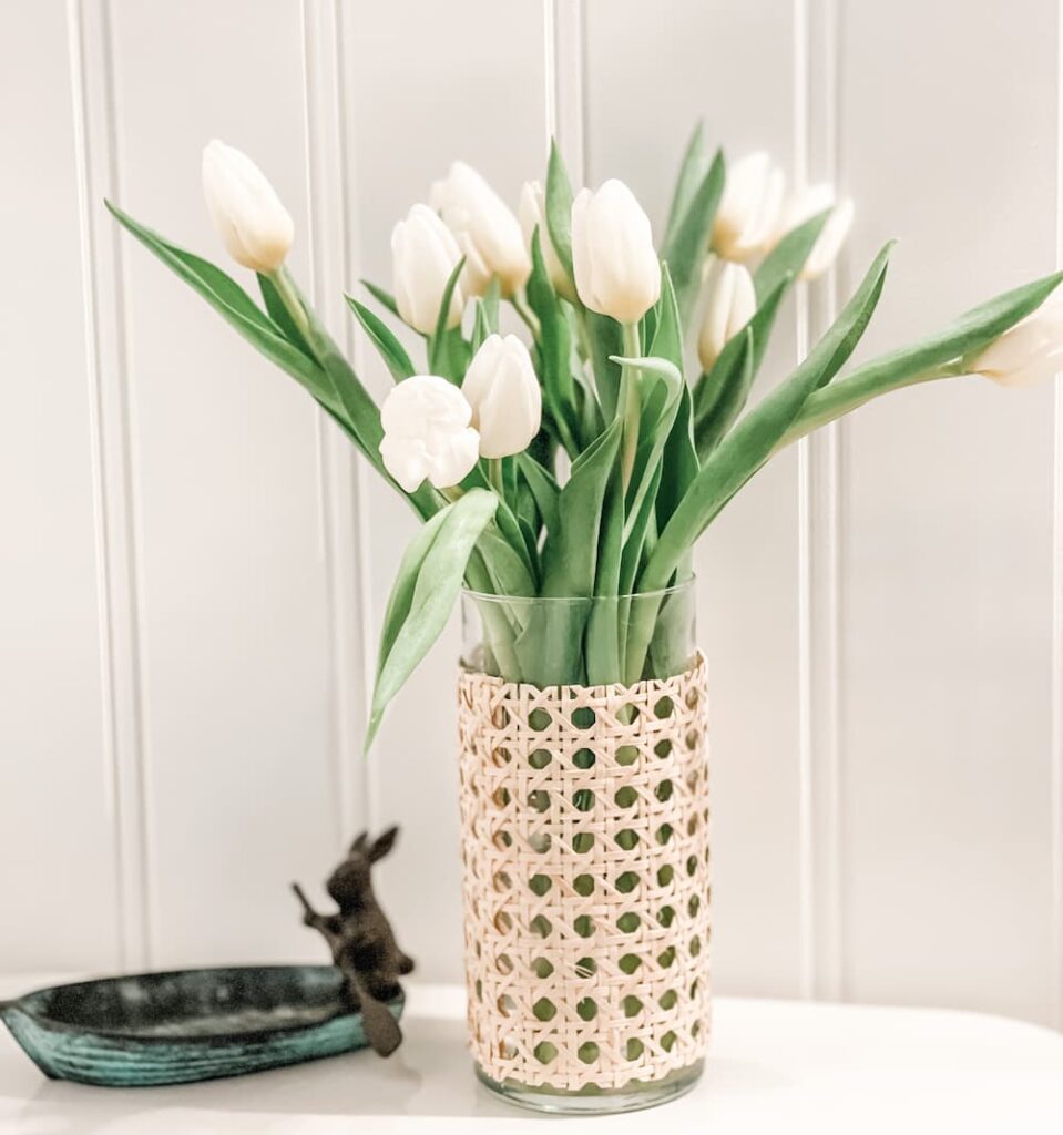 VASE COVERED WITH CANE FULL OF WHITE TULIPS NEXT TO A BUNNY IN A ROW BOAT