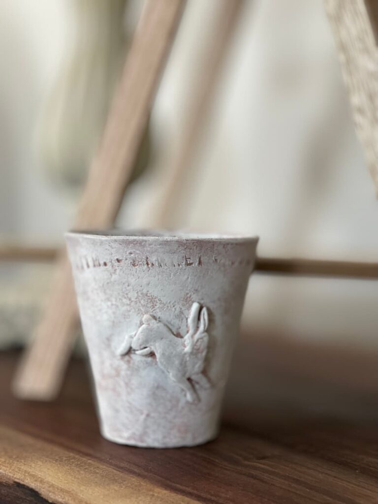 clay pot whitewashed with a small clay bunny on the outside.