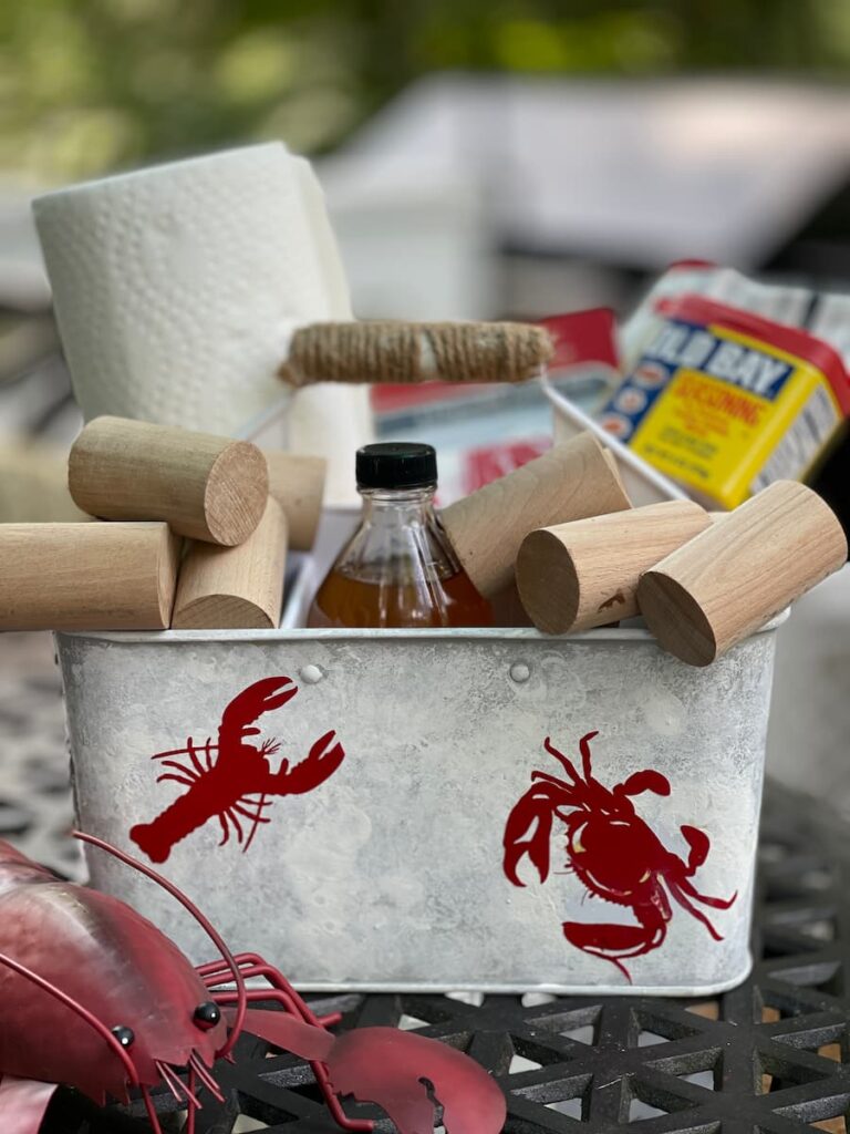 a silverware caddy with a crayfish and crab on the outside, filled with paper towels, knockers and seasonings for crabs